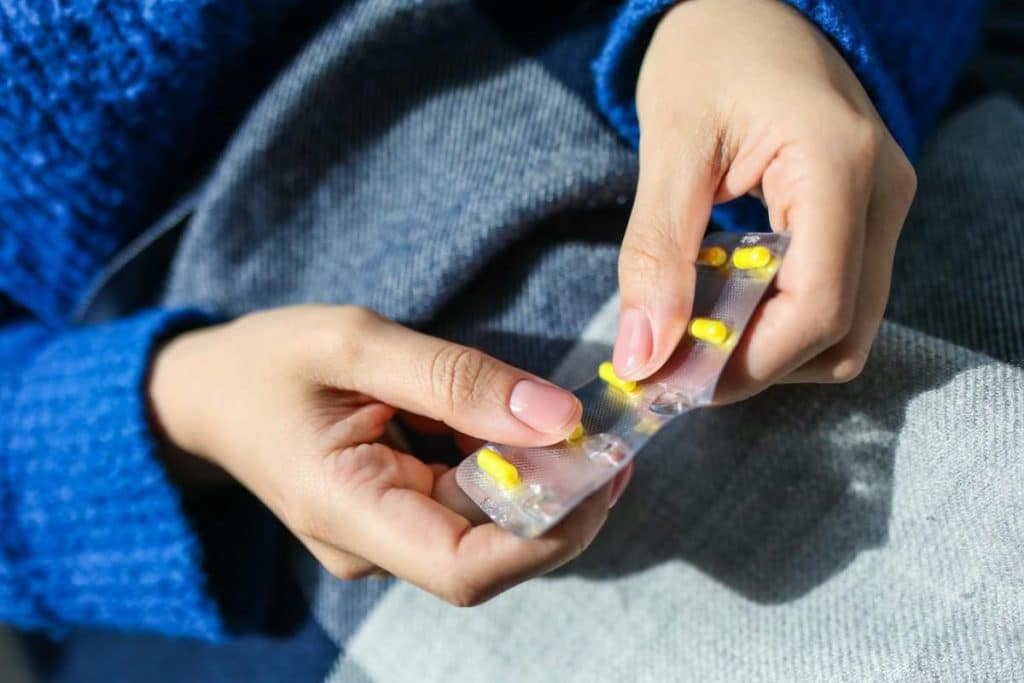 close up of a womans hands holding a blister pack with yellow pills indoors. 3873191 scaled (1)